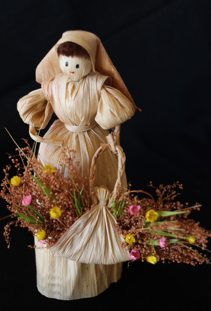 Corn doll carrying dried flowers in a basket.